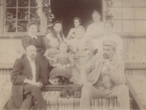 Fotografija. Evaldo ir Stanislavos Minichų šeima su savo artimaisiais nusipaveikslavę ant medinio namo prieangio laiptų. Apie 1910 m.