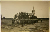 Daug kariškių su vėliava ir ginklais, žygiuoja prie bažnyčios aikštėje (nuotrauka)